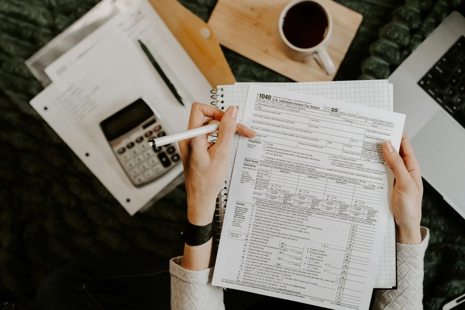 A person reviewing business paperwork with a calculator and laptop