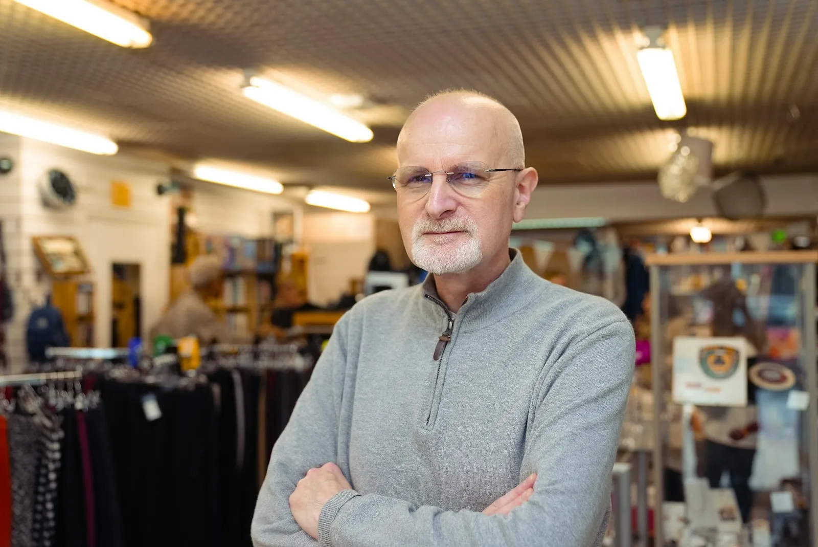A shop owner with glasses standing with his arms crossed in his clothing store