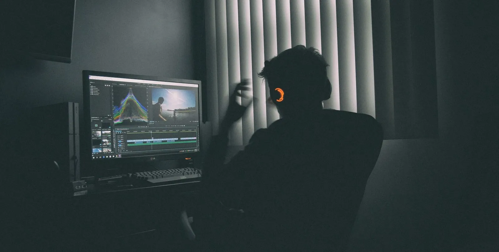 Person with headphones editing video on a computer in a dark room