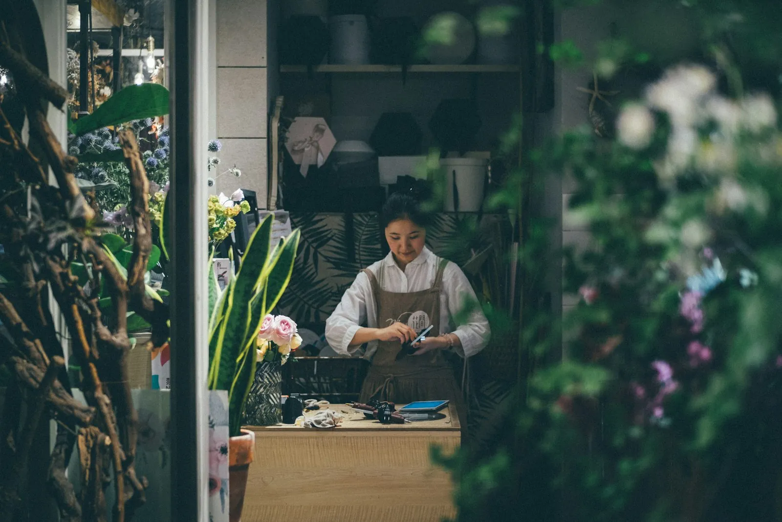 A florist checking her phone behind the counter of her flower shop